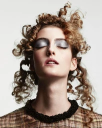 Close-up beauty portrait of a model with curly hair and metallic eyeshadow against a plain white background.