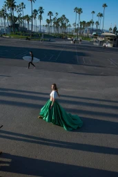 Model wearing a white top and voluminous green skirt on an asphalt plaza with palm trees in the background
