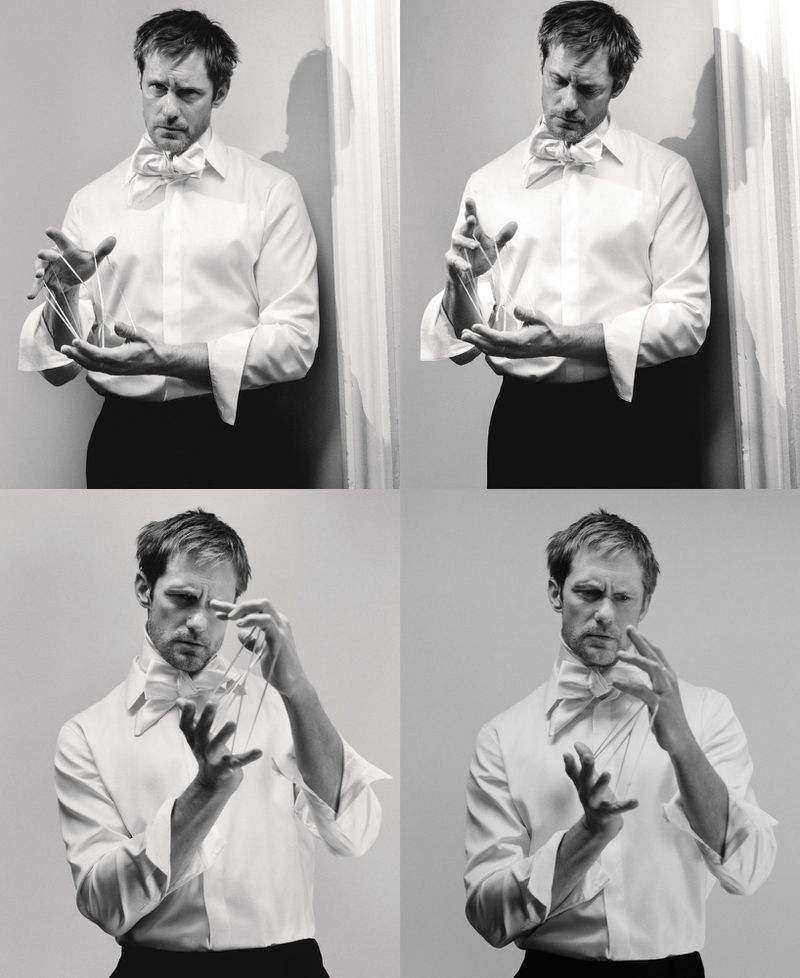 Black and white studio shot of an adult male wearing formal attire, holding clear string in his hands against a light wall background.