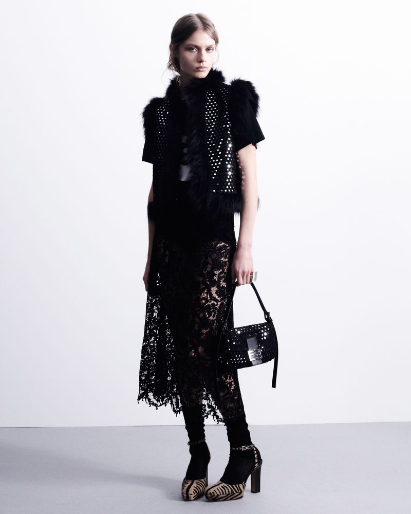 A fashion photo features a slender model in a black fur vest, lace skirt, handbag, and heels against a stark white backdrop.