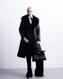 Model in black fur collar coat holding patterned handbag against white background