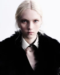 Close-up portrait of a blonde model wearing a white collared shirt and black fur coat against a white background
