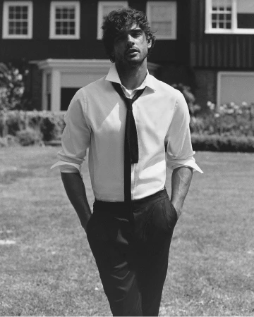 Black and white portrait of a man in a white shirt and tie outdoors with a house and lawn in the background on a sunny day.