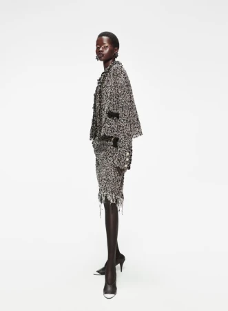 Fashion shot of an African woman posing in a tweed jacket and skirt, standing in a white photo studio in black heels.