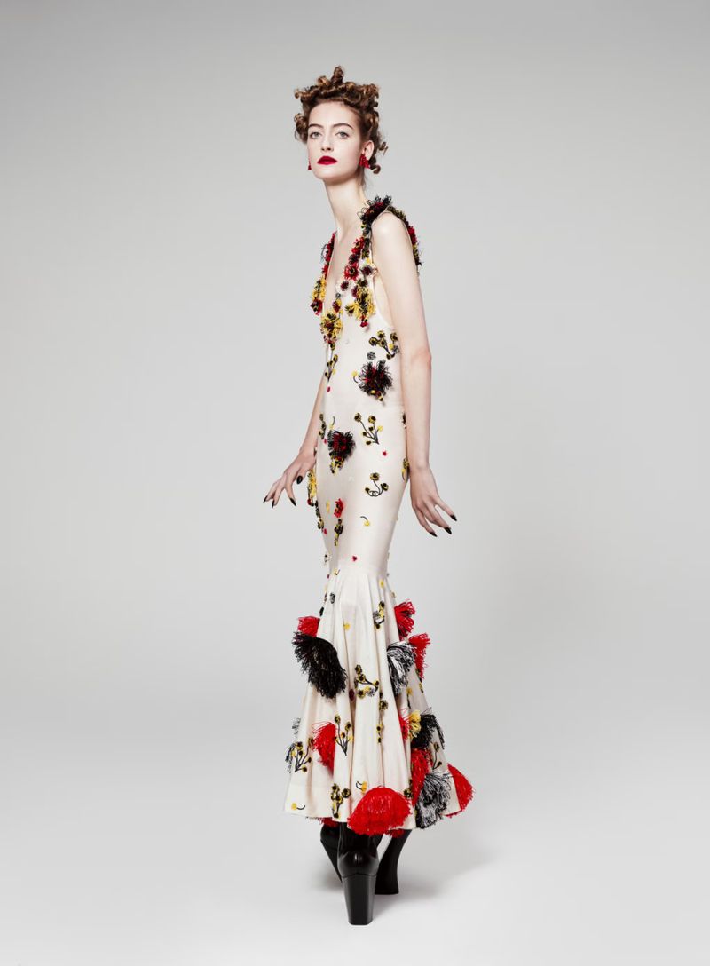 Elegant adult female poses in a floral-embellished gown with a fishtail design and chunky boots, set against a plain studio background.