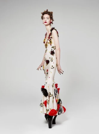 Elegant adult female poses in a floral-embellished gown with a fishtail design and chunky boots, set against a plain studio background.