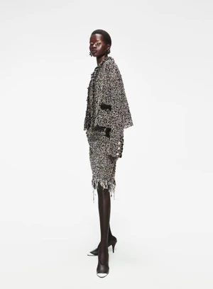 Model wearing a textured tweed jacket and skirt standing against a plain white background for Elle U.S.