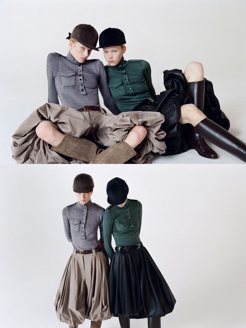 Two fashion models pose in a studio wearing riding caps, form-fitting tops, and distinctive skirts, exhibiting a high-fashion equestrian style.