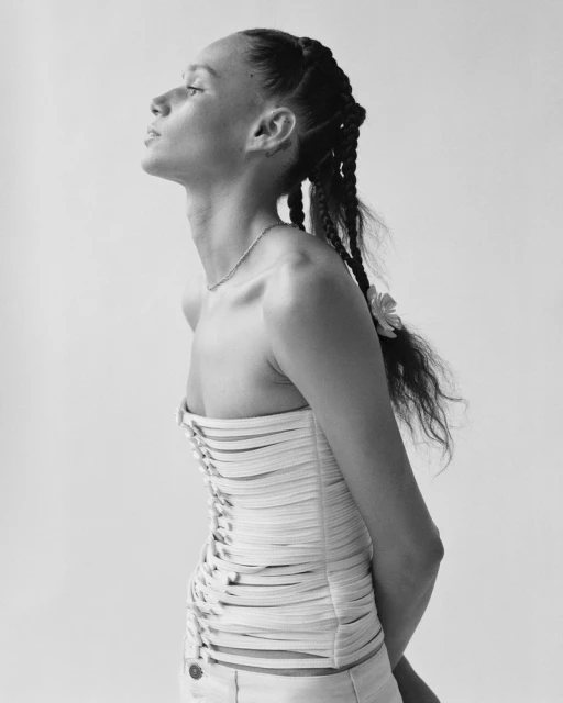 Black and white portrait of a woman with braided hair wearing a strapless top, shot in a photo studio with a plain white backdrop.