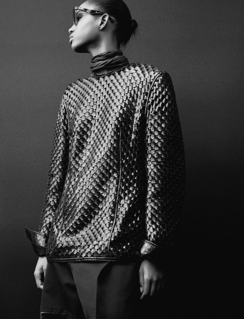 Black and white portrait of a fashion model wearing a textured long-sleeve shirt, paired with dark pants and statement sunglasses.