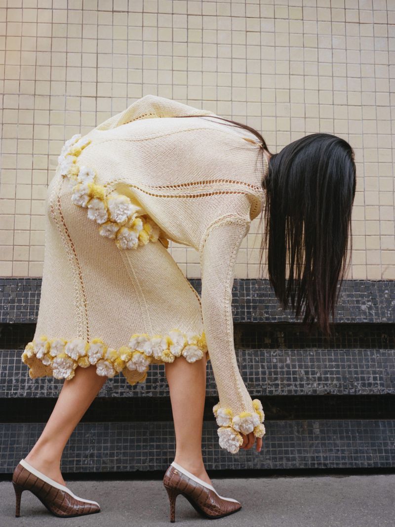 Fashion shot of a woman wearing a cream-colored knit skirt and sweater with flower details, accessorized with brown and white high heels.