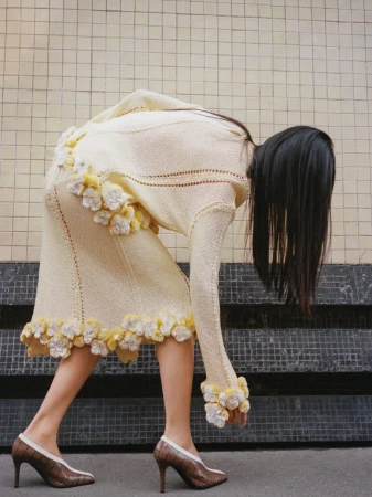 Fashion shot of a woman wearing a cream-colored knit skirt and sweater with flower details, accessorized with brown and white high heels.