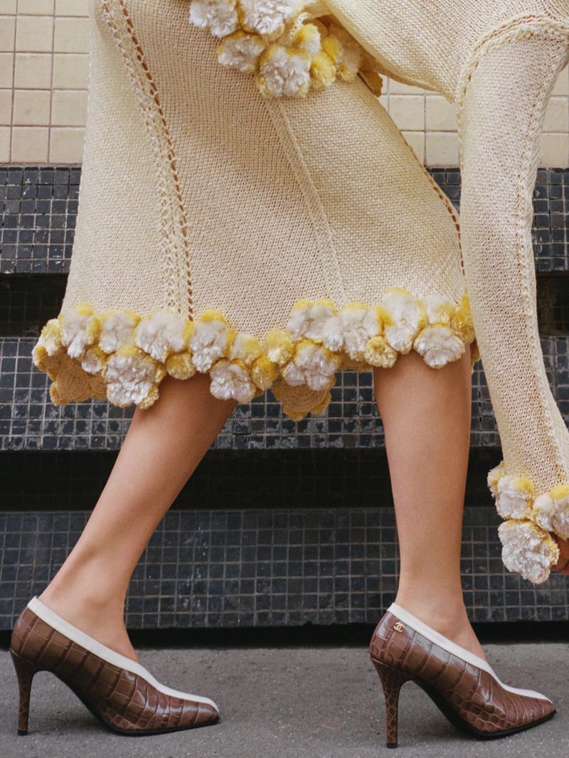 Close-up on a woman modeling a cream-colored knit dress with floral accents, paired with brown and cream crocodile-print high-heeled pumps on concrete.