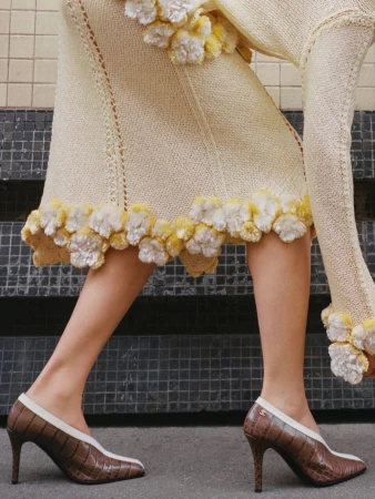 Close-up on a woman modeling a cream-colored knit dress with floral accents, paired with brown and cream crocodile-print high-heeled pumps on concrete.