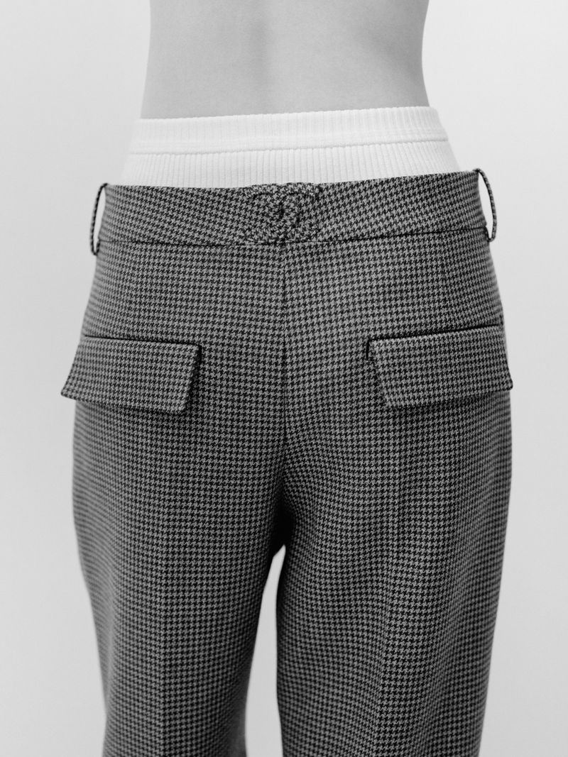 Close-up rear view of houndstooth patterned trousers with back pockets and a white waistband against a neutral background.