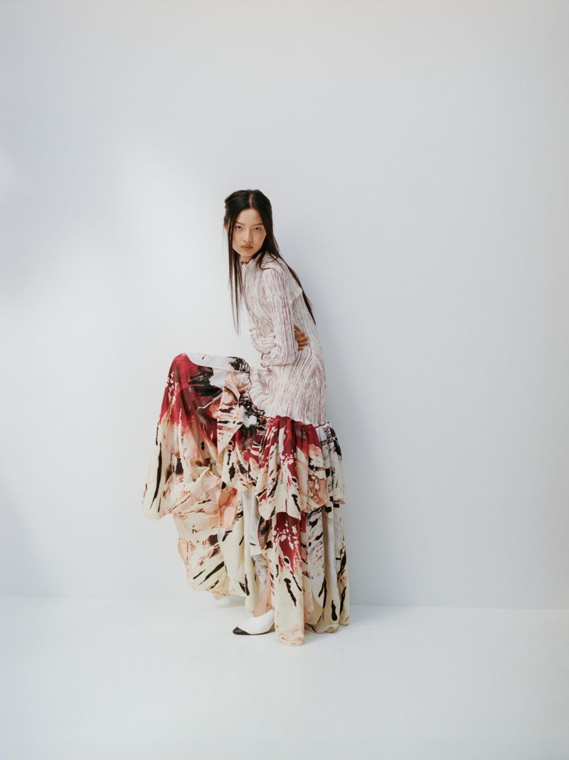 Full-length shot of a woman posing in a studio wearing a light pink and white patterned dress with a tiered ruffle skirt.