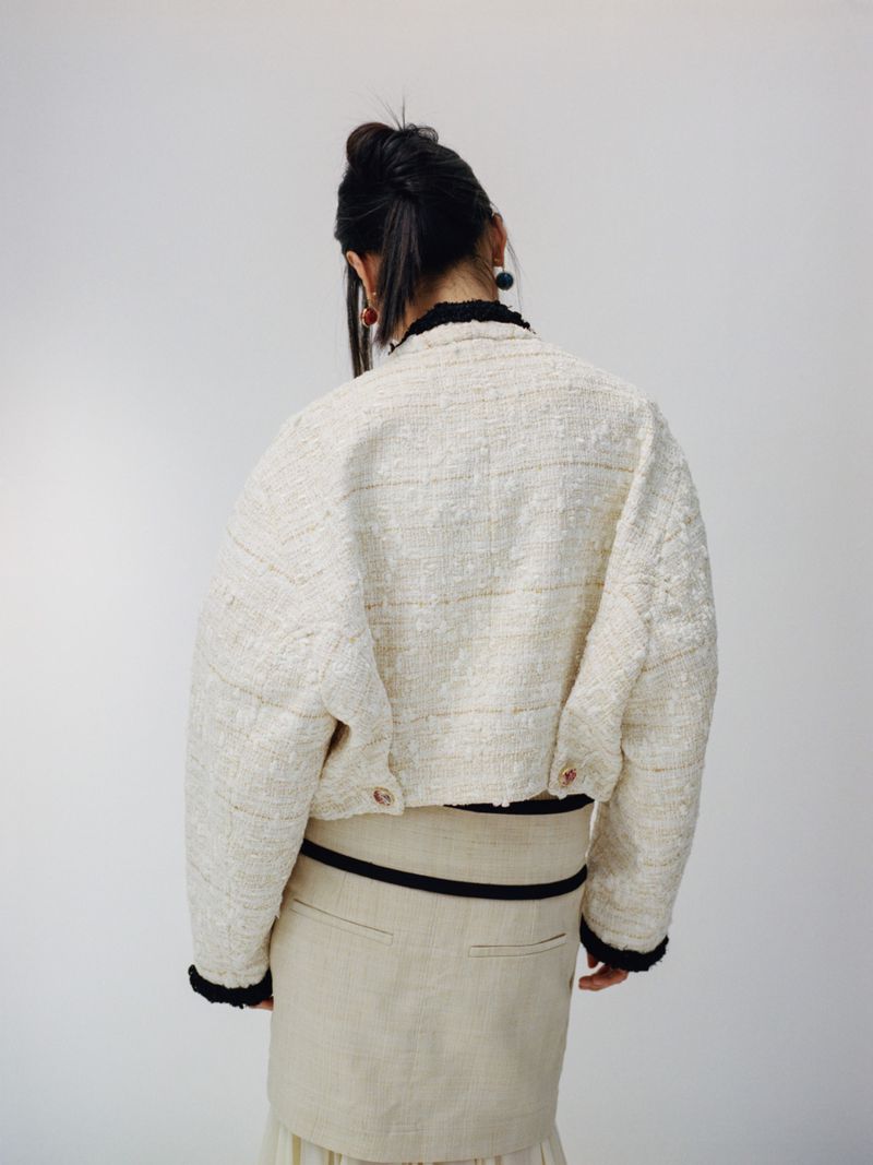 Woman in stylish cream-colored tweed jacket and skirt posing in a bright studio. Back view highlights the jacket's texture and fit.