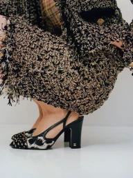 Model wearing a textured tweed jacket and patterned heels against a plain white studio backdrop.