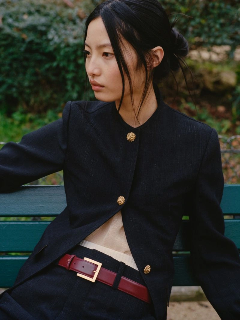 Model Chen Yang wearing a black jacket with gold buttons seated on a green park bench for Muse Magazine editorial photographed by Sasha Marro.