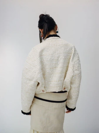Model from behind wearing a textured cream tweed jacket and beige skirt against a white background