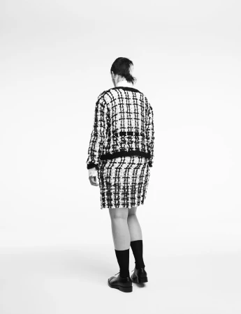 Model from behind wearing a black and white tweed jacket and matching skirt against a white studio background.