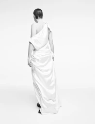 Model with short hair seen from behind wearing a white one-shoulder gown against a plain white background