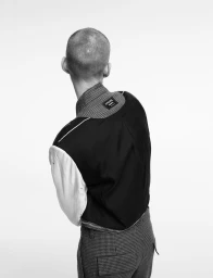 Model seen from behind wearing a black and white tailored jacket and patterned trousers against a white backdrop.