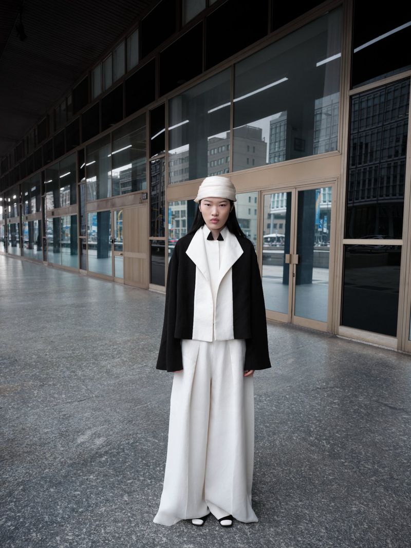 Fashionable Asian woman in a black and white outfit stands in an urban setting with a bucket hat, cropped jacket, and wide-leg pants.