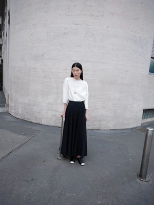 Asian woman in white top and black skirt standing against a curved stone building exterior.