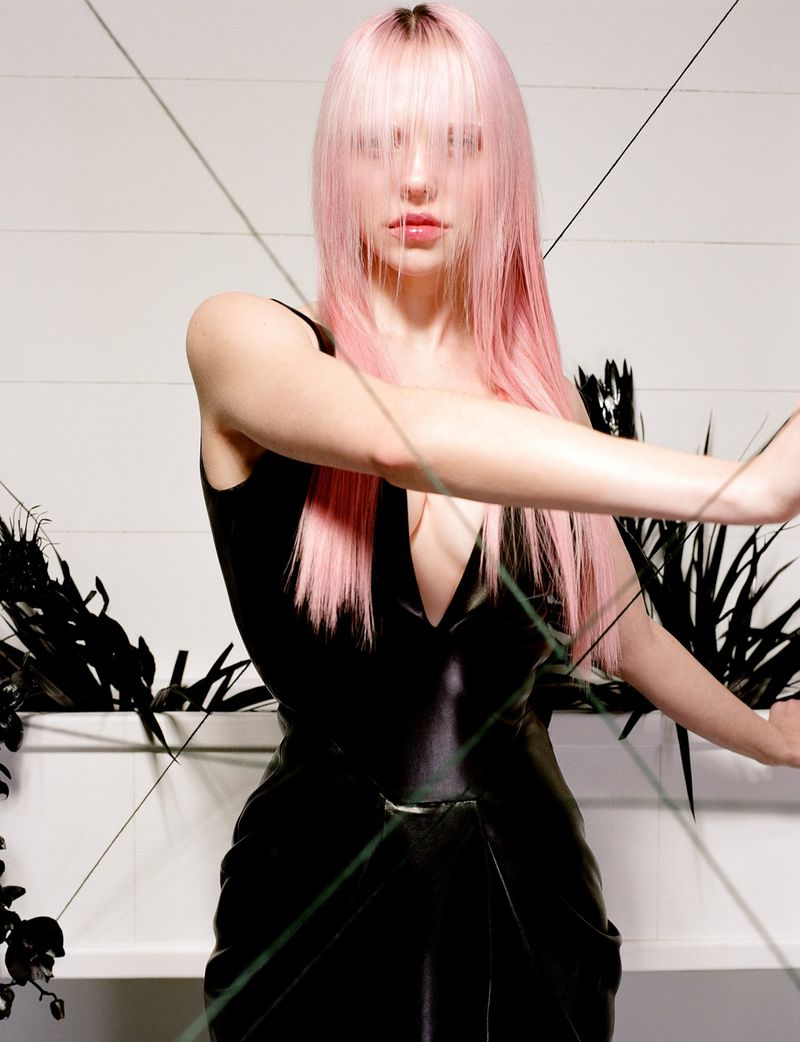 A fair-skinned woman with light pink hair poses in a black dress against a white background with linear decorations and floral arrangements.