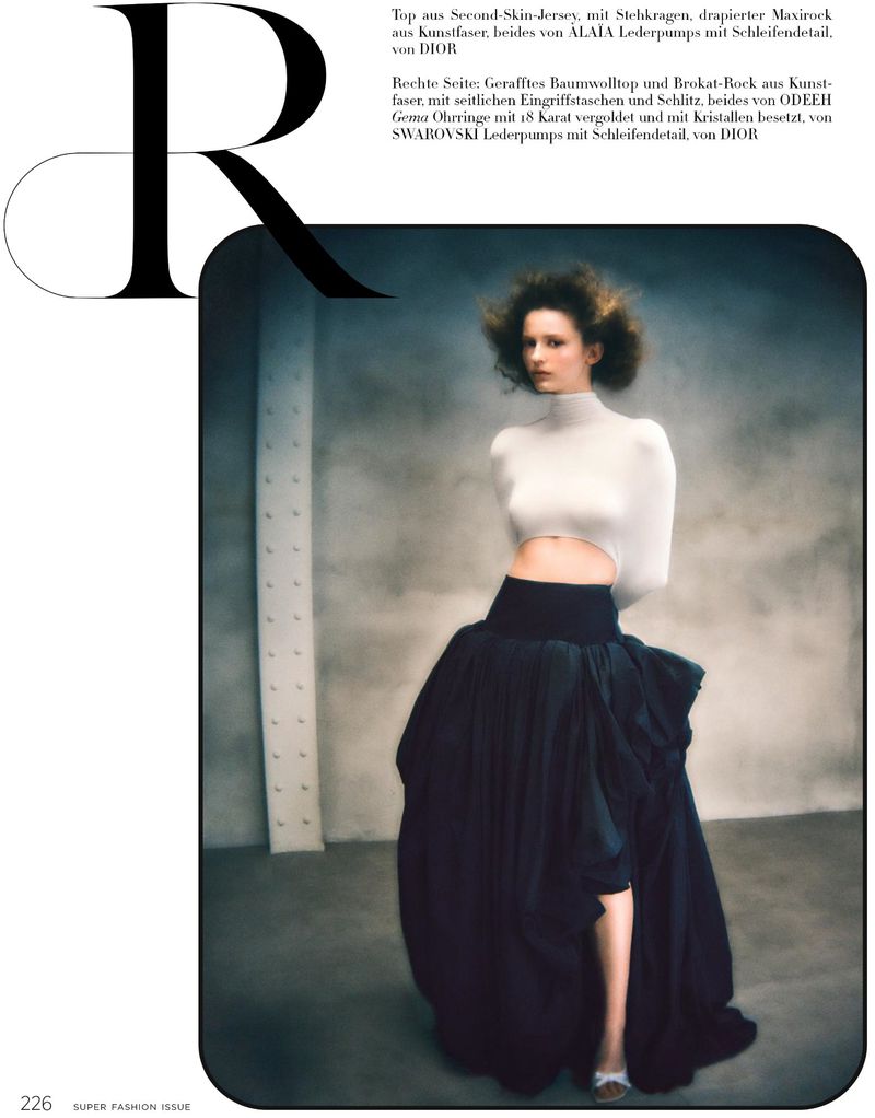 Model wearing a white crop top and dark maxi skirt standing against a textured industrial concrete wall background.