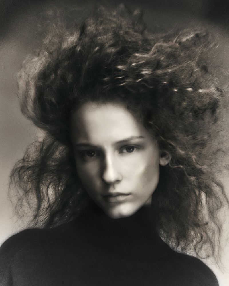 Portrait of a model with voluminous curly hair wearing a dark turtleneck sweater against a neutral background