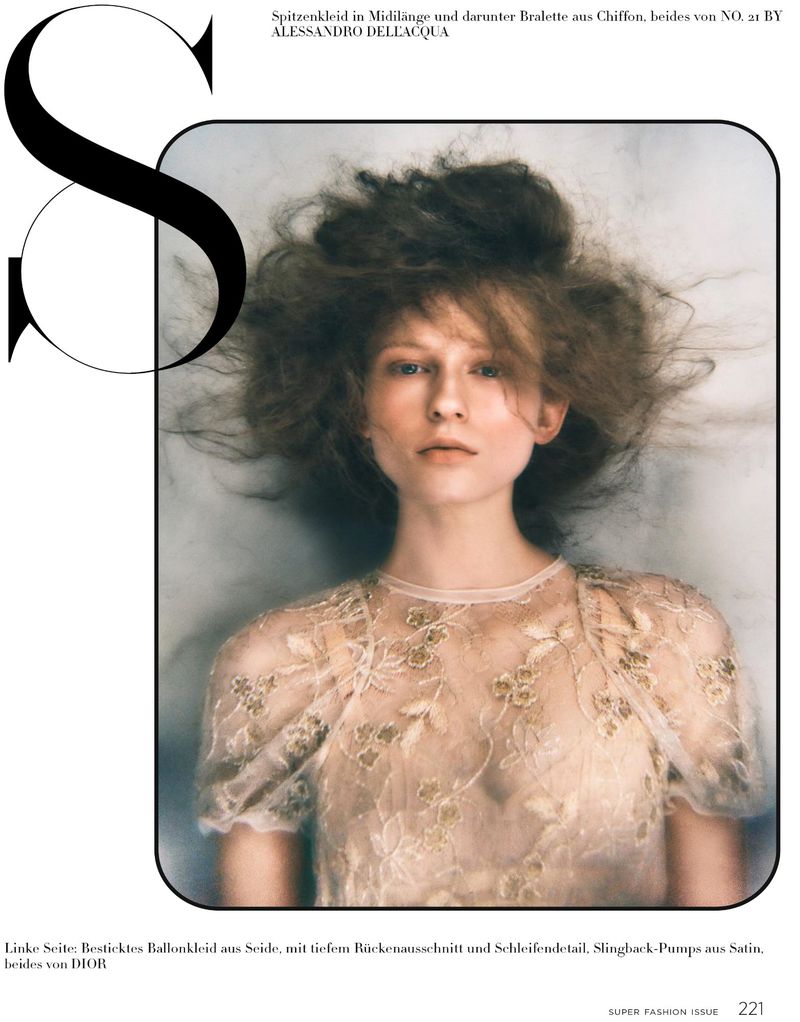 Close-up fashion shot of a fair-skinned model wearing an embroidered sheer blouse and with an updo hairstyle against a blurry grey background.