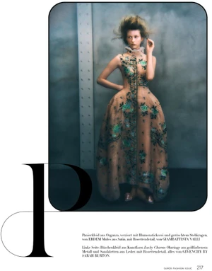 Model wearing a sheer embroidered gown with structured panniers standing against an industrial textured wall