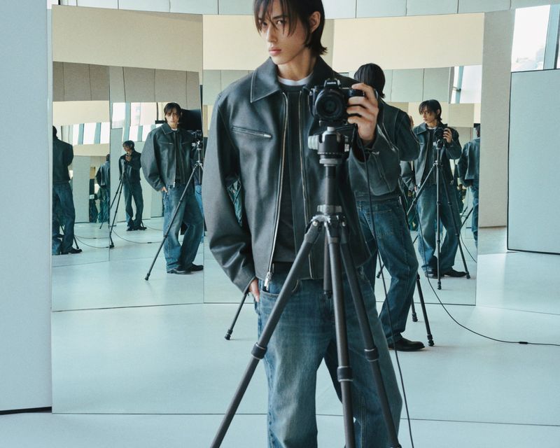 Adult male takes a selfie with a camera on a tripod in a photo studio with multiple mirror reflections showing a casual fashion style.