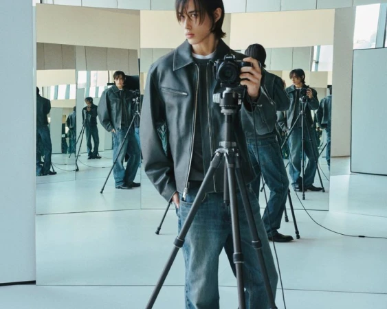 Adult male takes a selfie with a camera on a tripod in a photo studio with multiple mirror reflections showing a casual fashion style.