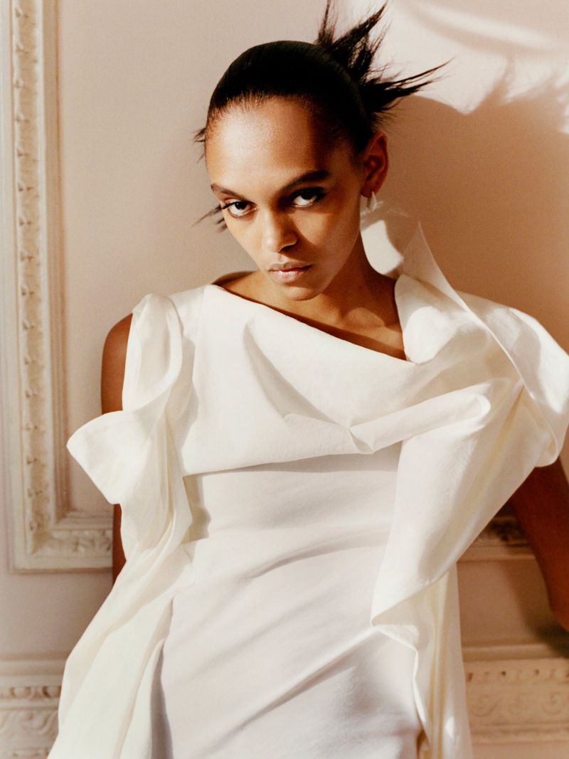 Elegant fashion portrait of an adult woman in a white ruffled dress, captured indoors in a photo studio with a soft lighting style.