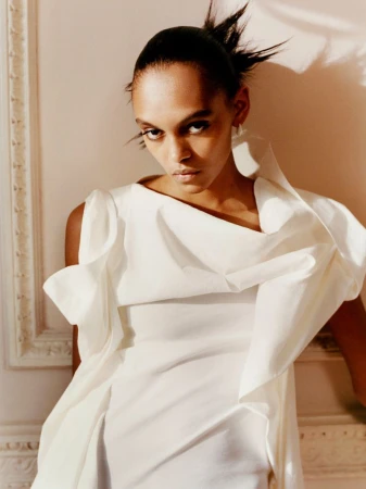 Model Bebe Parnell wearing a sculptural white dress against an ornate interior wall for T Magazine