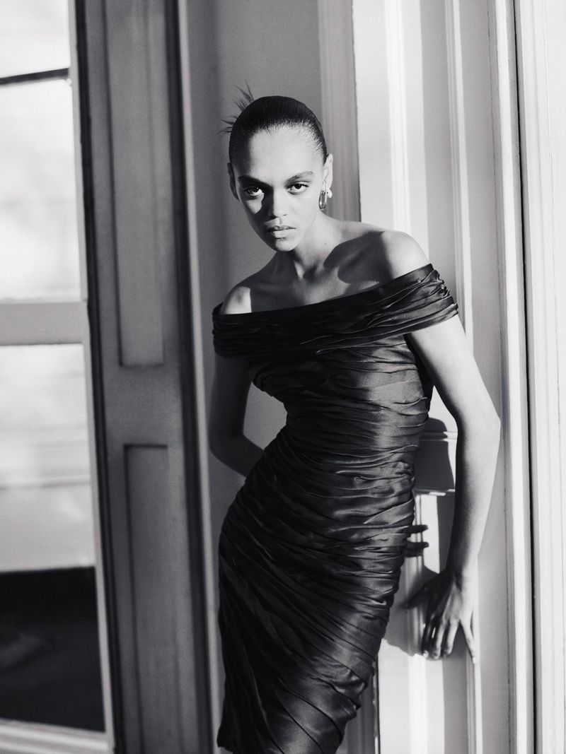 Model in an off-the-shoulder black dress posing near architectural pillars in a monochrome editorial photograph