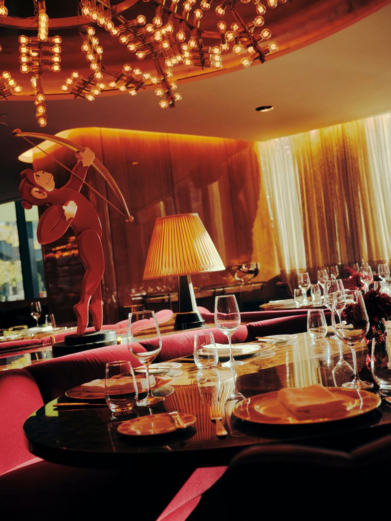 Elegant restaurant interior with a dining table set for service, a red Cupid statue, artistic light fixture, and warm golden lighting.