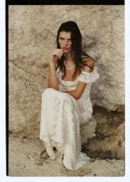 Model in white lace wedding dress sitting against rocky coastal background for Self-Portrait Bridal SS26 editorial