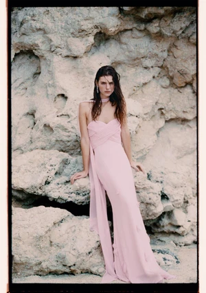 Model wearing a pale pink strapless gown leaning against a rough rock formation outdoors