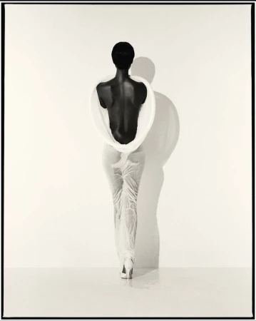Elegant, back-facing view of a slender African-American woman in light clothing and high heels, standing against a bright background.