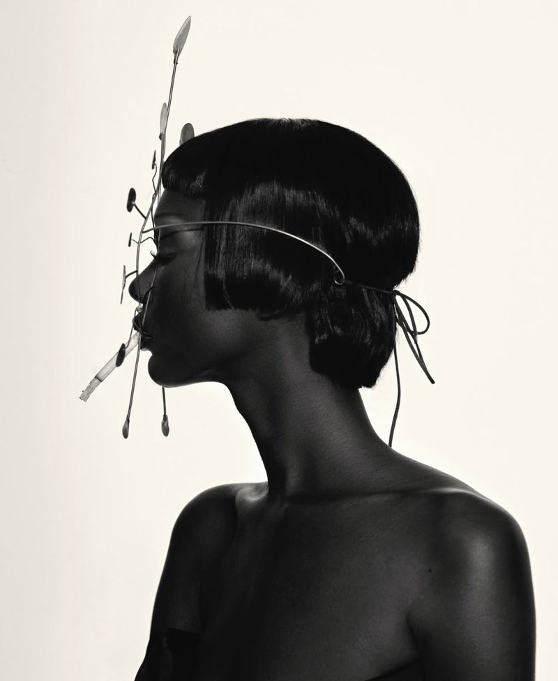 Striking profile portrait of a dark-skinned female model with a sleek black bob hairstyle and an elaborate artistic metal headpiece in studio.