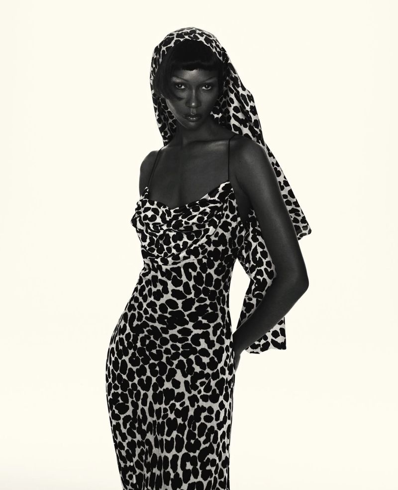 Elegant Black woman poses in a form-fitting, floor-length dress with an all-over leopard print, complemented by a matching headscarf.
