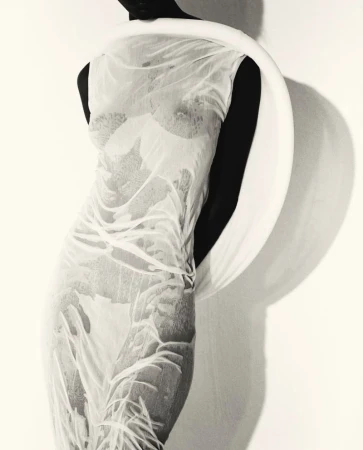 Model Mahany Pery in a sheer textured dress wearing a sculptural white neck ring against a white background for Elle Brasil