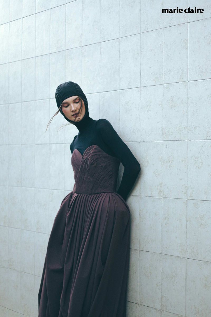 A woman in a formal gown and head covering leans against a textured wall, fashion photography, studio shot for Marie Claire magazine.