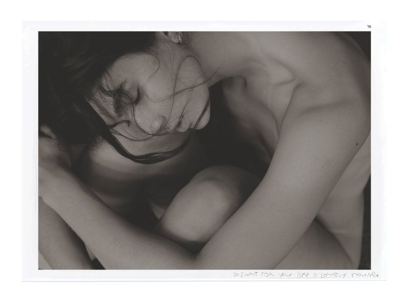 Monochrome portrait of a nude adult woman with closed eyes and dark hair, her arms embracing her legs.