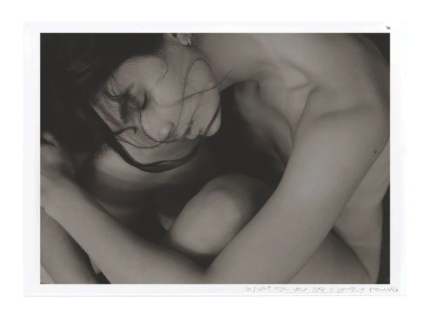 Monochrome portrait of a nude adult woman with closed eyes and dark hair, her arms embracing her legs.