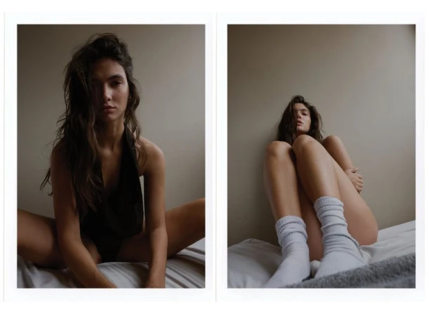 Indoor portrait of a young woman with wavy hair in two poses on a white bed, wearing a black top and white socks against a neutral wall.